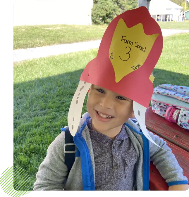 A young boy wearing a paper hat in the grass.